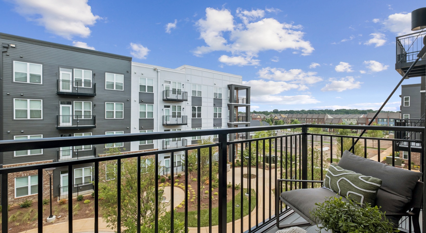 Inviting apartment balcony with cozy seating and a scenic view of modern architecture and lush greenery, perfect for relaxation at The Rowley in Murfreesboro