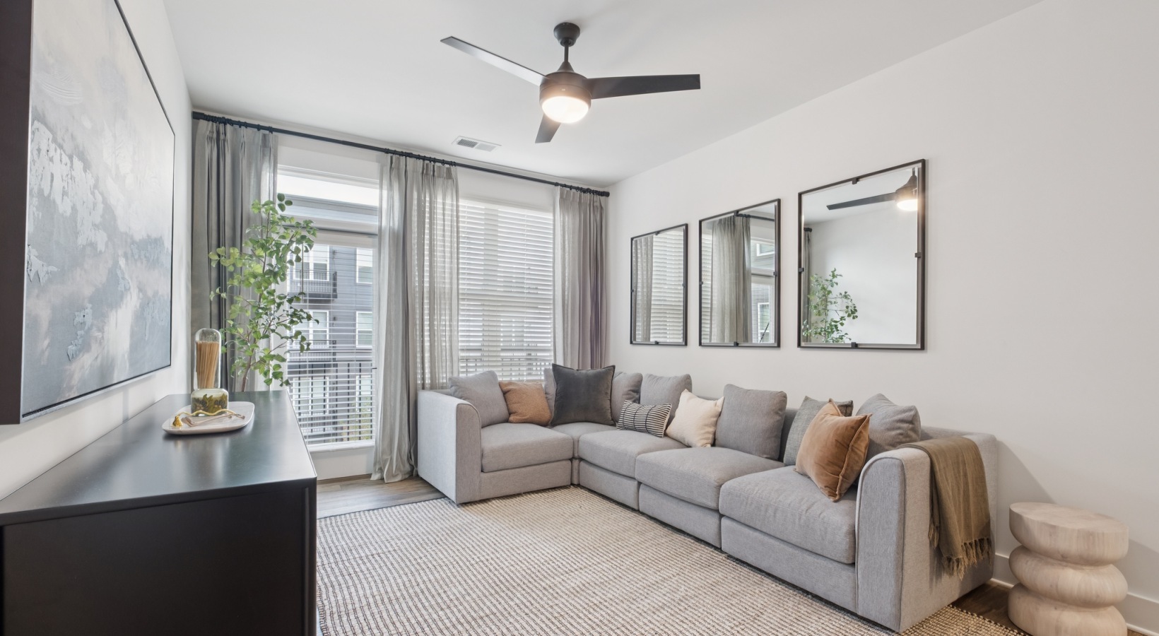 Bright and modern living room featuring a cozy gray sectional sofa, elegant decor, and large windows with flowing curtains, offering an inviting and stylish space at The Rowley in Murfreesboro