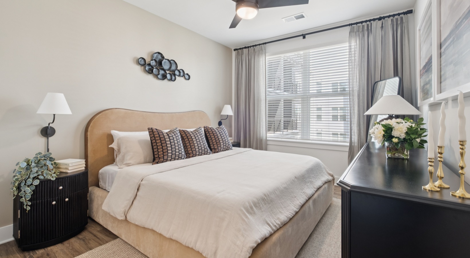 Elegant bedroom showcasing a cozy beige bed with stylish patterned pillows, modern decor, and ample natural light from large windows at The Rowley in Murfreesboro.