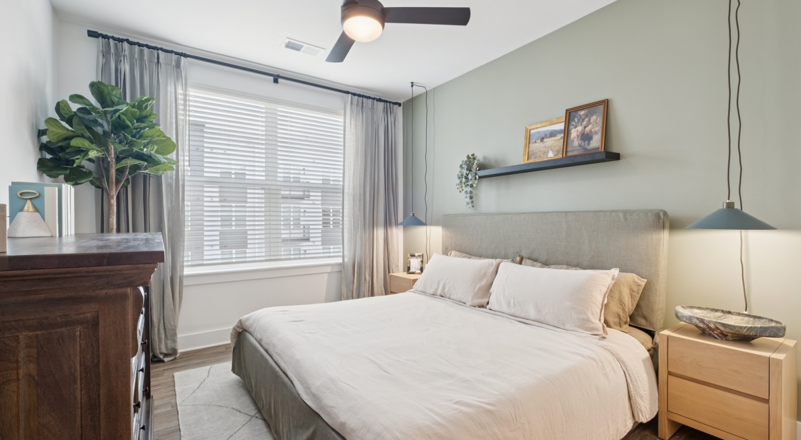 Inviting bedroom with soft green accent wall, elegant ceiling fan, and abundant natural light at The Rowley in Murfreesboro.