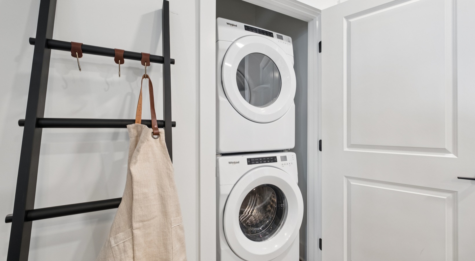 Contemporary laundry nook with sleek stackable washer and dryer, accentuated by a stylish black ladder rack and a minimalist beige apron at The Rowley in Murfreesboro