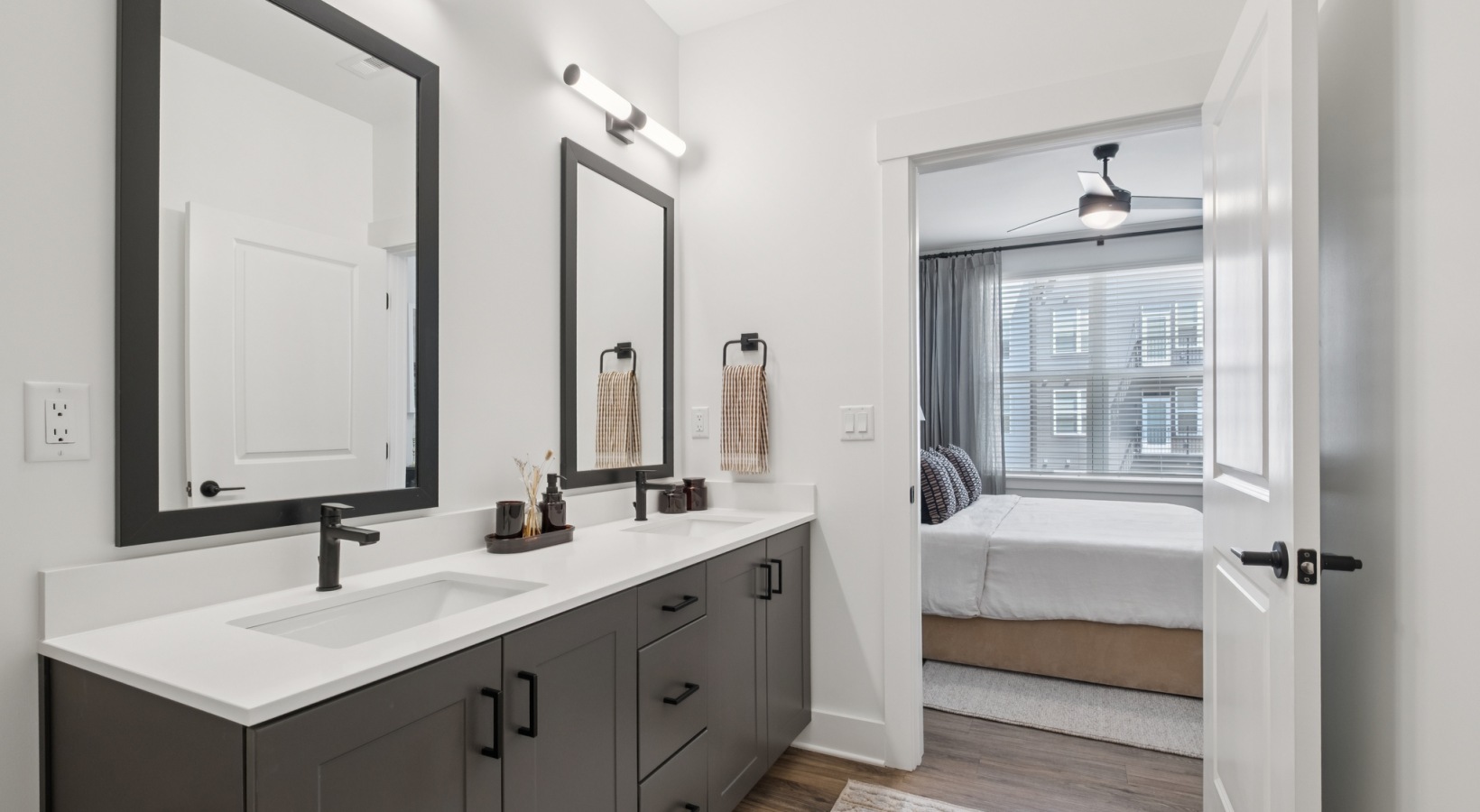 Modern bathroom featuring dual sinks with elegant mirrors and contemporary fixtures, leading to a cozy bedroom with ample natural light at The Rowley in Murfreesboro.