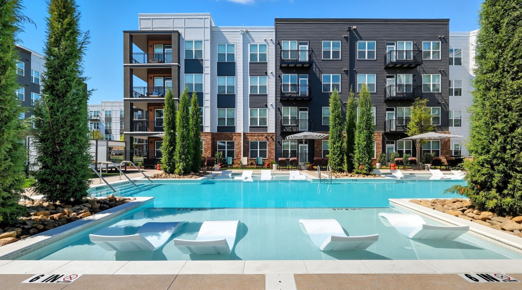 Dive in and cool off in the sparkling pool Modern apartment complex with a luxurious swimming pool and stylish poolside loungers, surrounded by lush greenery under a vibrant blue sky at The Rowley in Murfreesboro