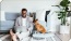 a person sitting on a couch with a laptop and a dog